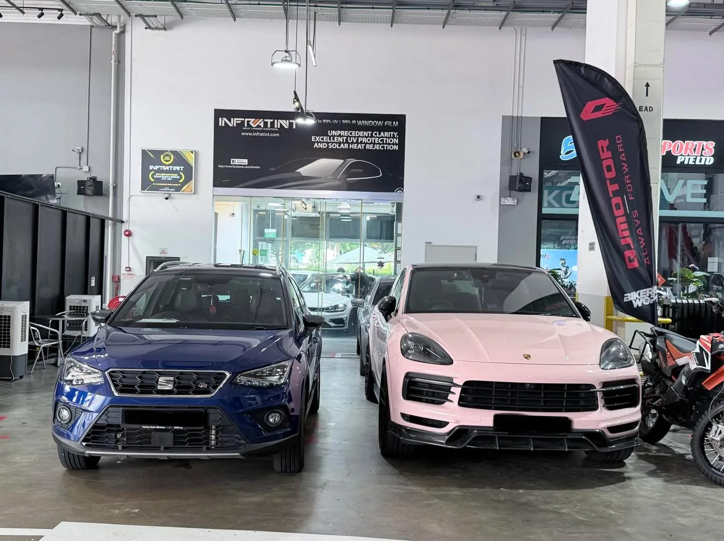 A blue Seat SUV and a pink Porsche Cayenne parked at the workshop.