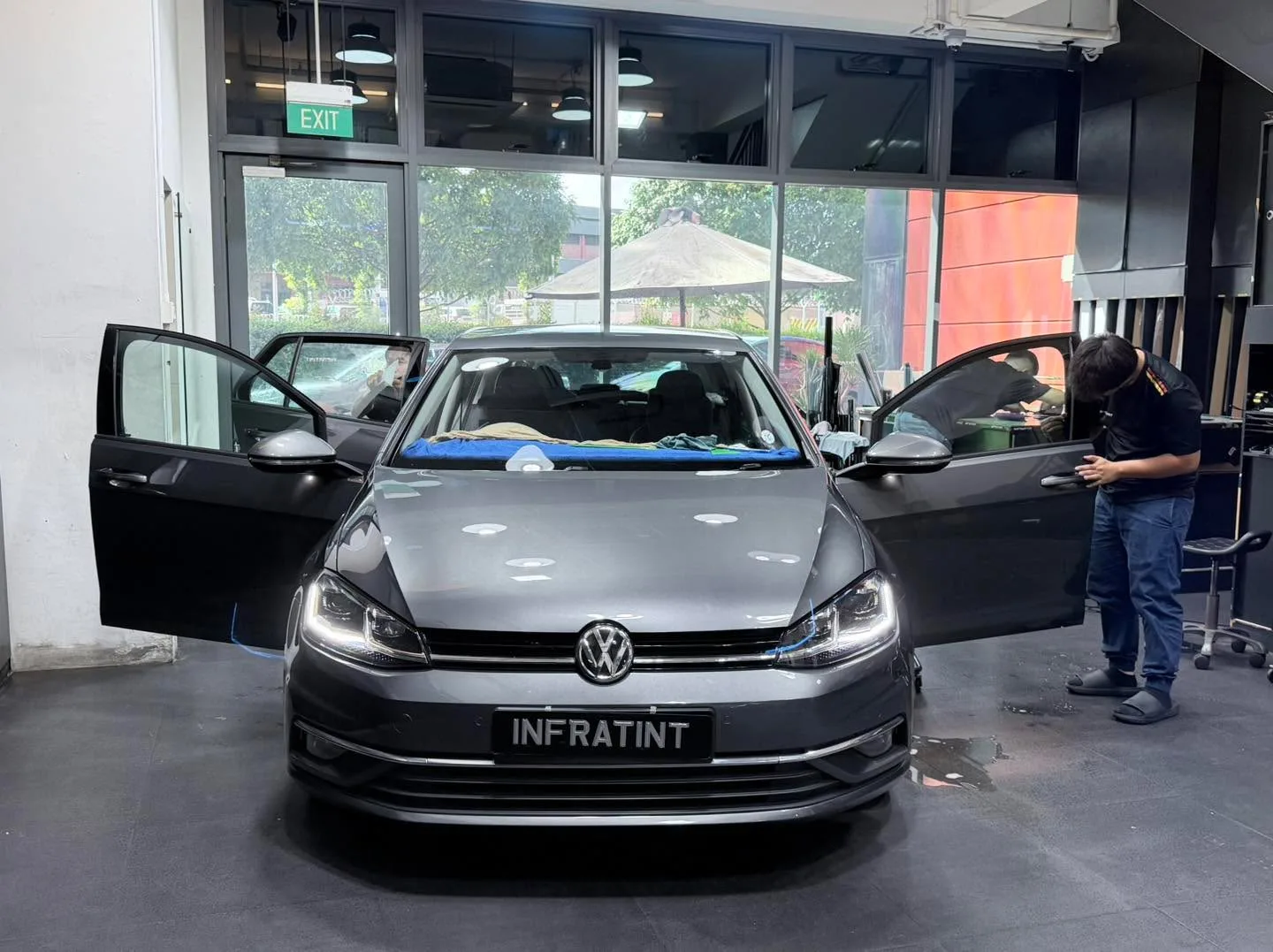 A grey Volkswagen Golf with doors open during window tinting work.