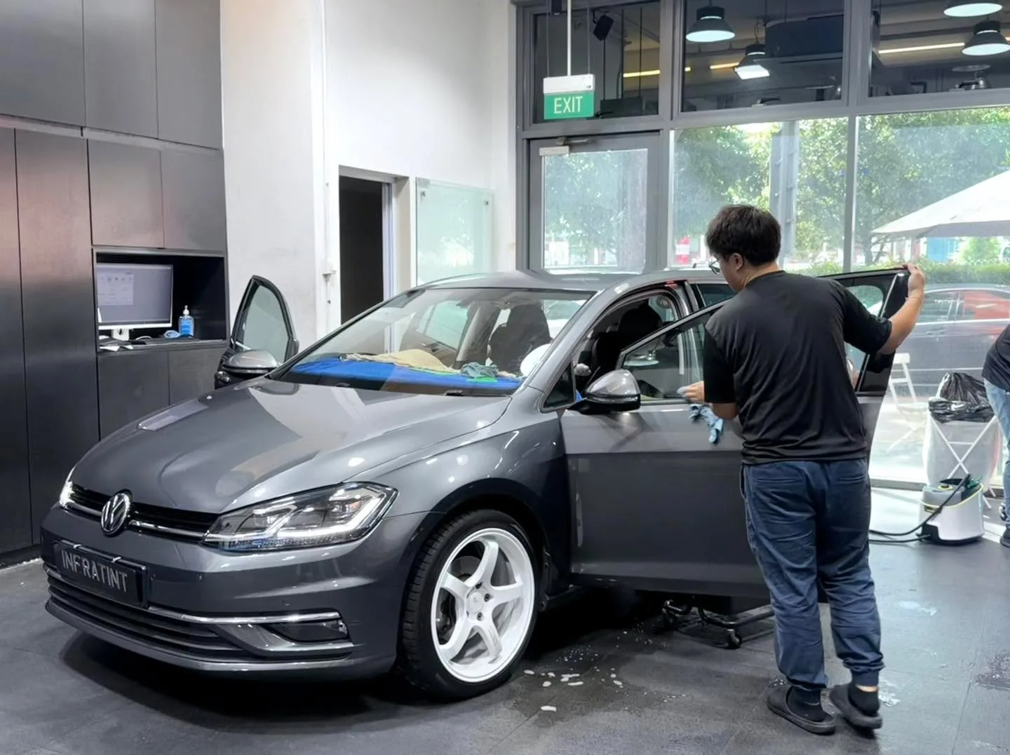 A grey Volkswagen Golf with door open and a technician applying window film.
