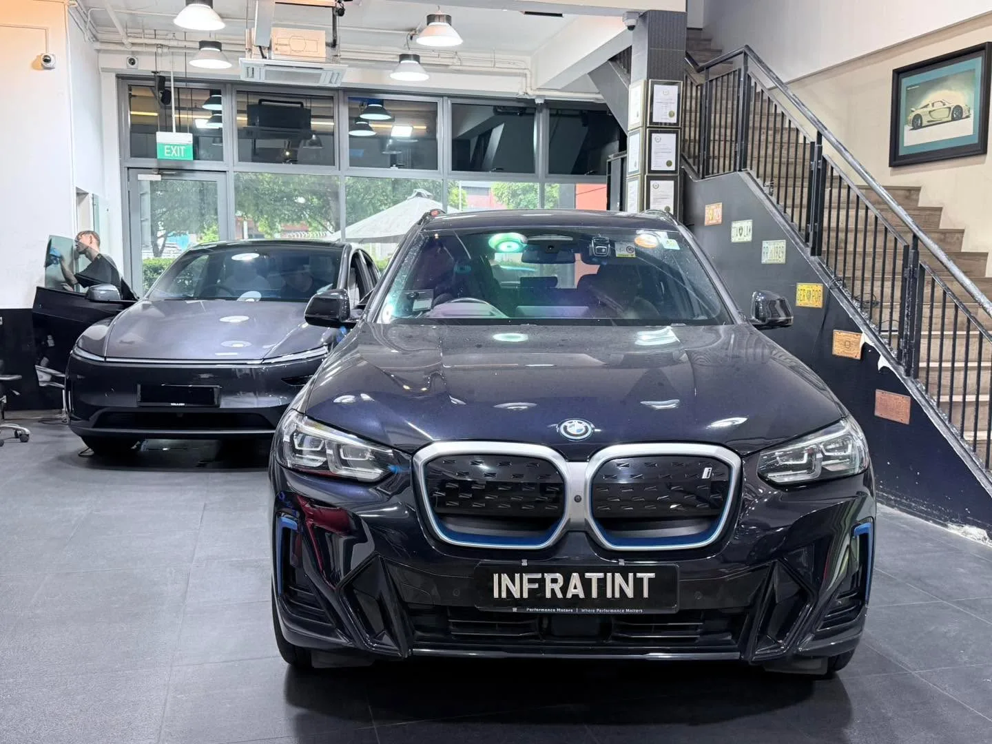 A black BMW iX3 with distinctive twin grilles faces the camera in the workshop.