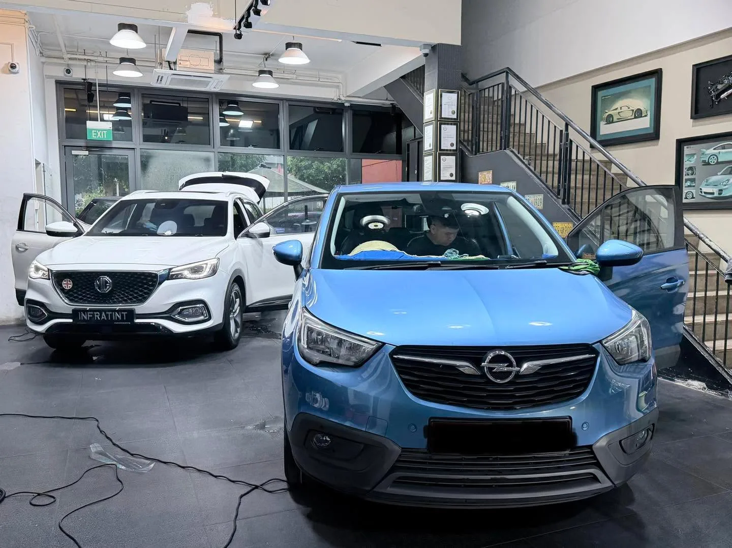 A white MG SUV and blue Opel Crossland are parked side by side in the workshop.