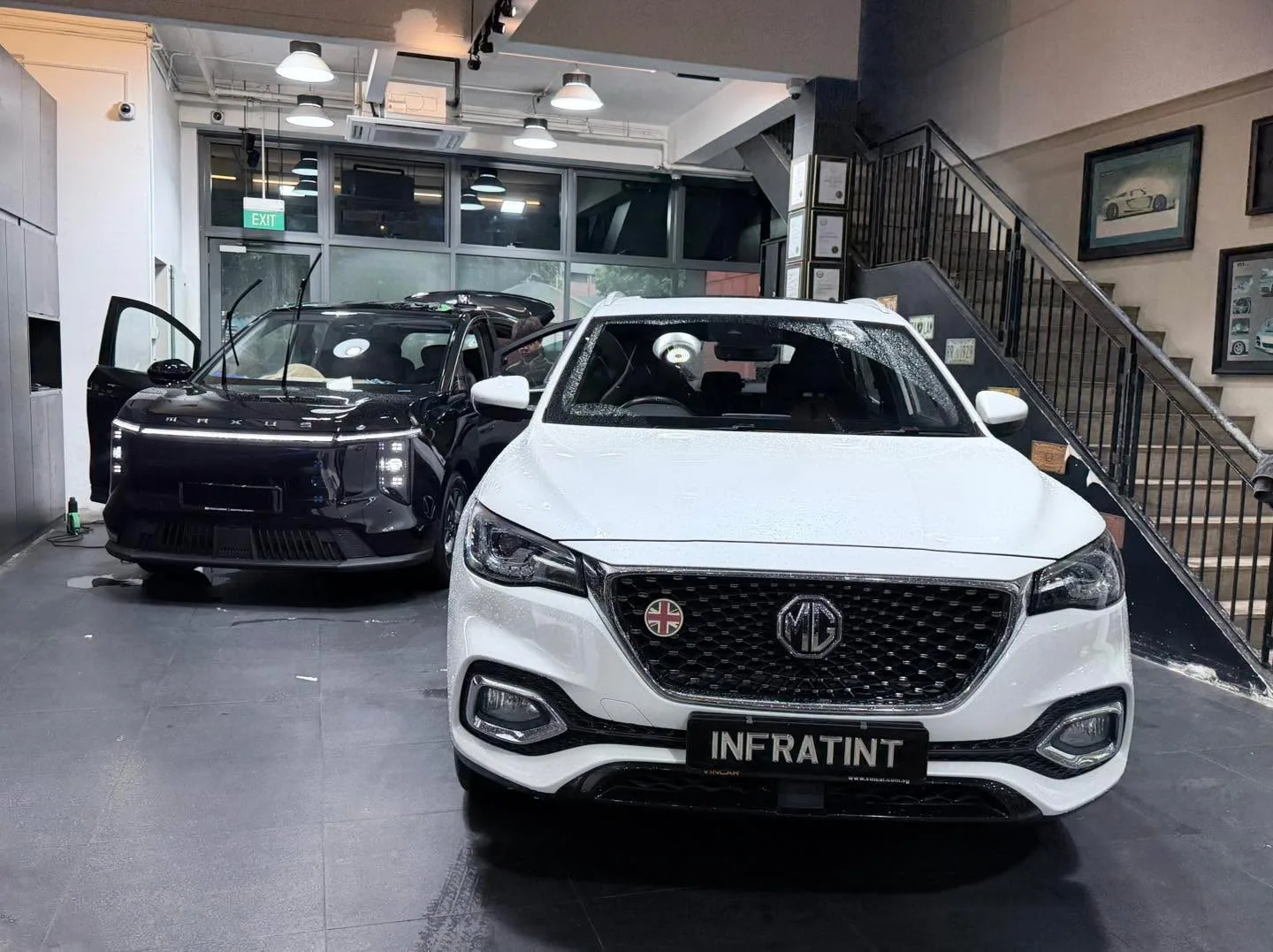 A white MG SUV in foreground and black electric vehicle with open door in background.