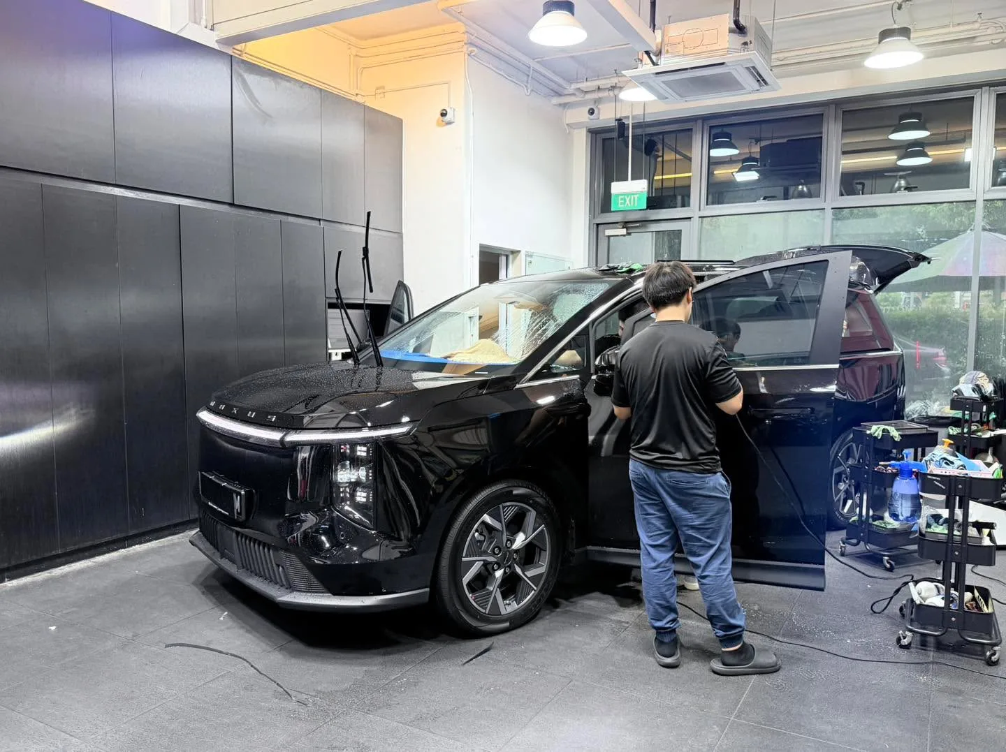 A dark-coloured electric sedan with open doors in the workshop during tinting.