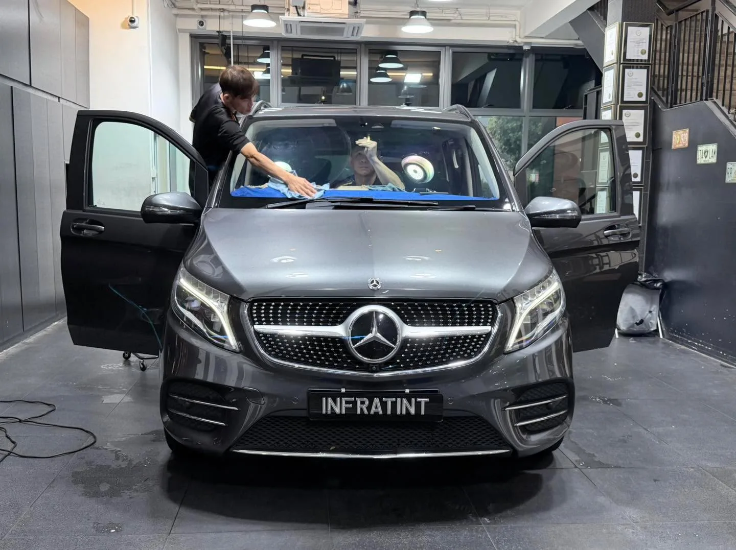 A grey sedan with technician applying window tint film to the windscreen.