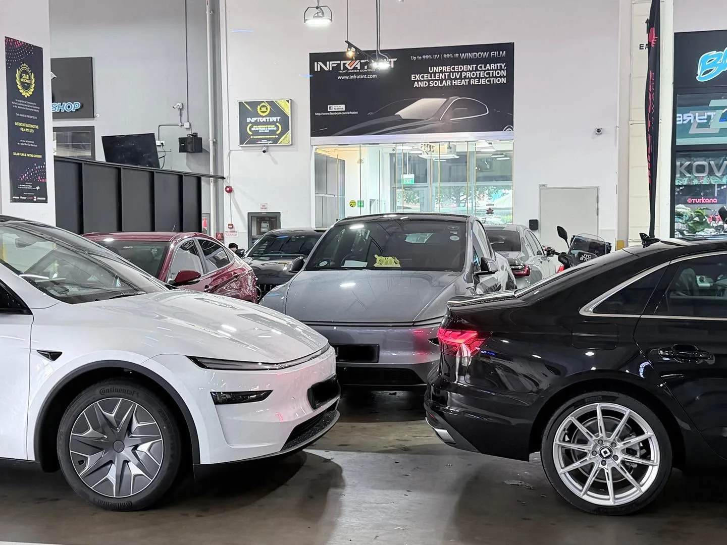A white electric SUV and a black sedan parked among other vehicles in the workshop.