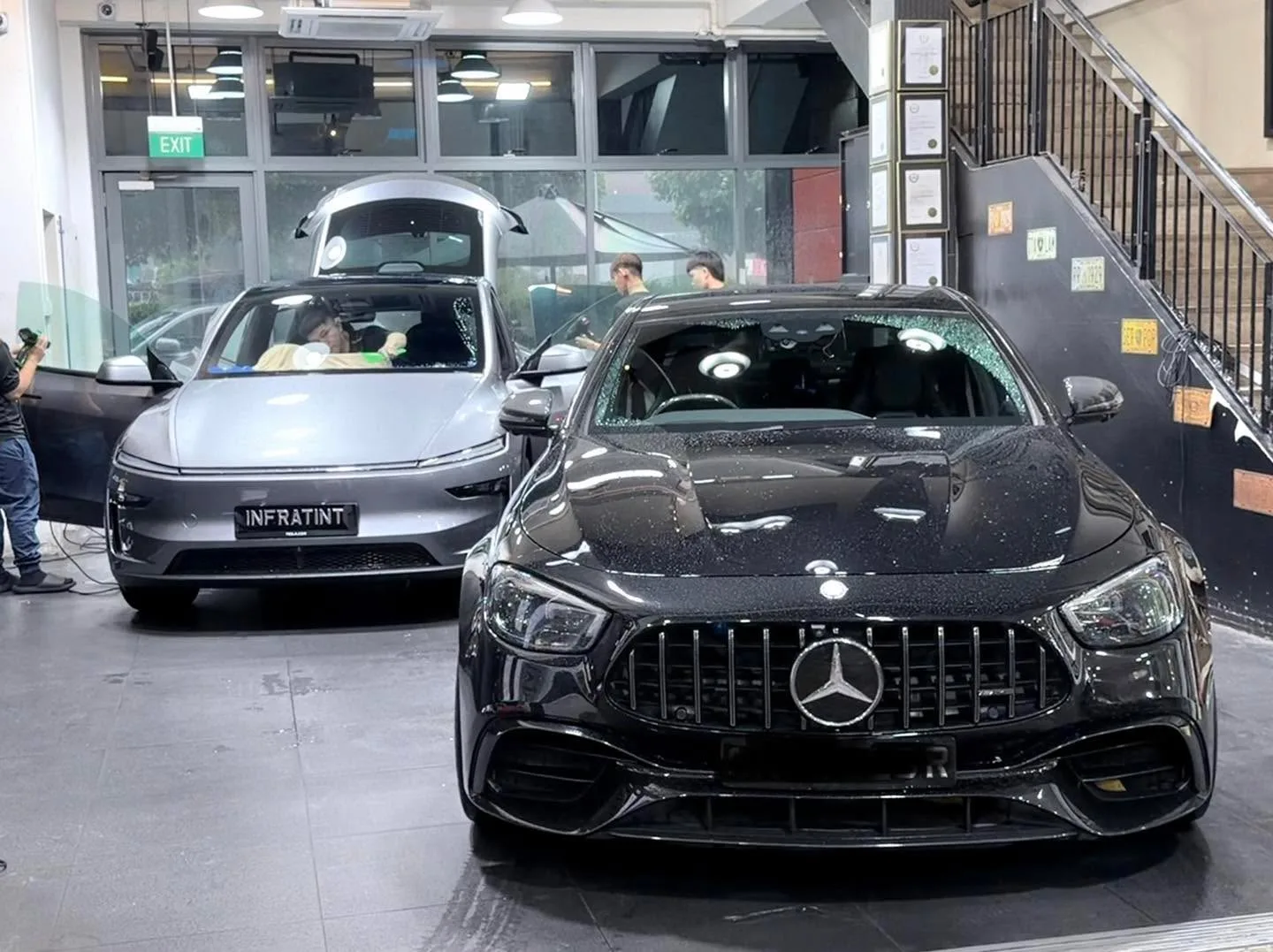 A black Mercedes sedan with distinctive grille and a silver Tesla sedan inside the workshop.