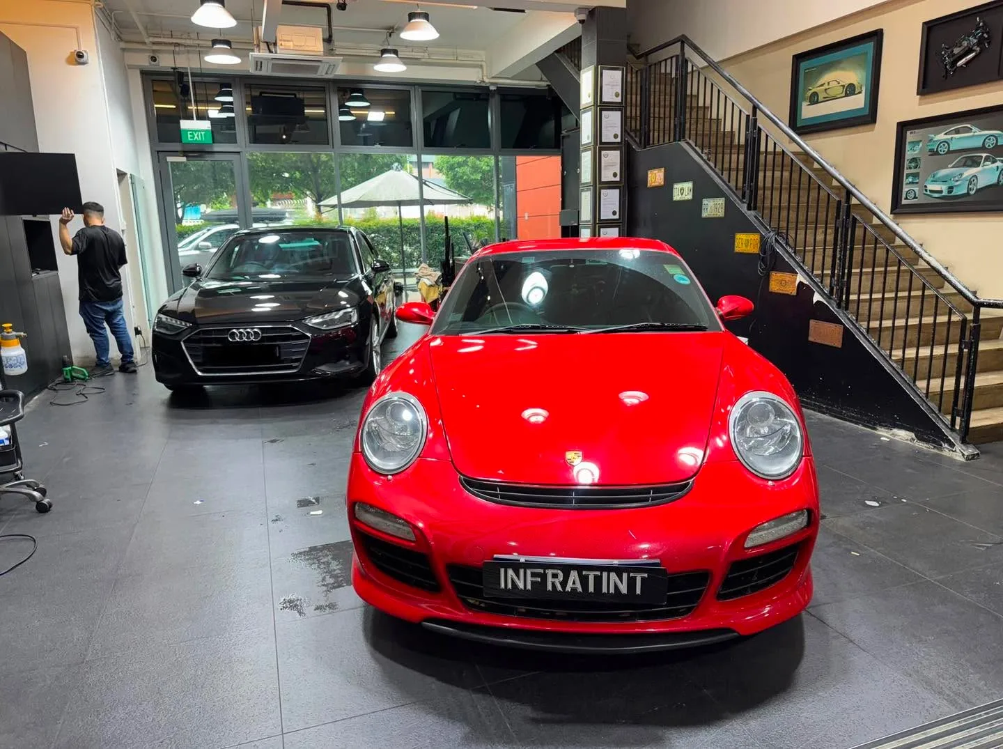 A red Porsche sports car in the foreground with a dark Audi sedan to the left.