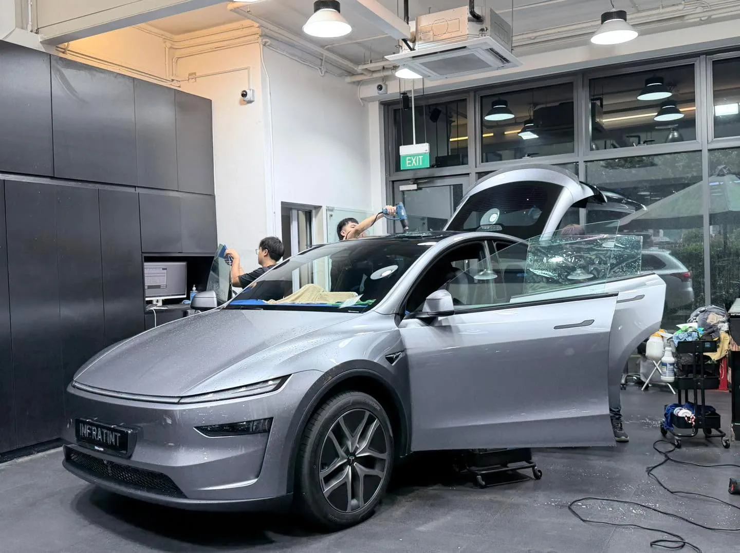 A silver Tesla electric hatchback with open door during tinting work inside the workshop.
