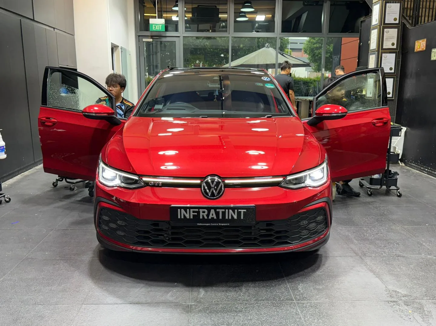 A red Volkswagen hatchback with open doors inside the workshop during tinting.