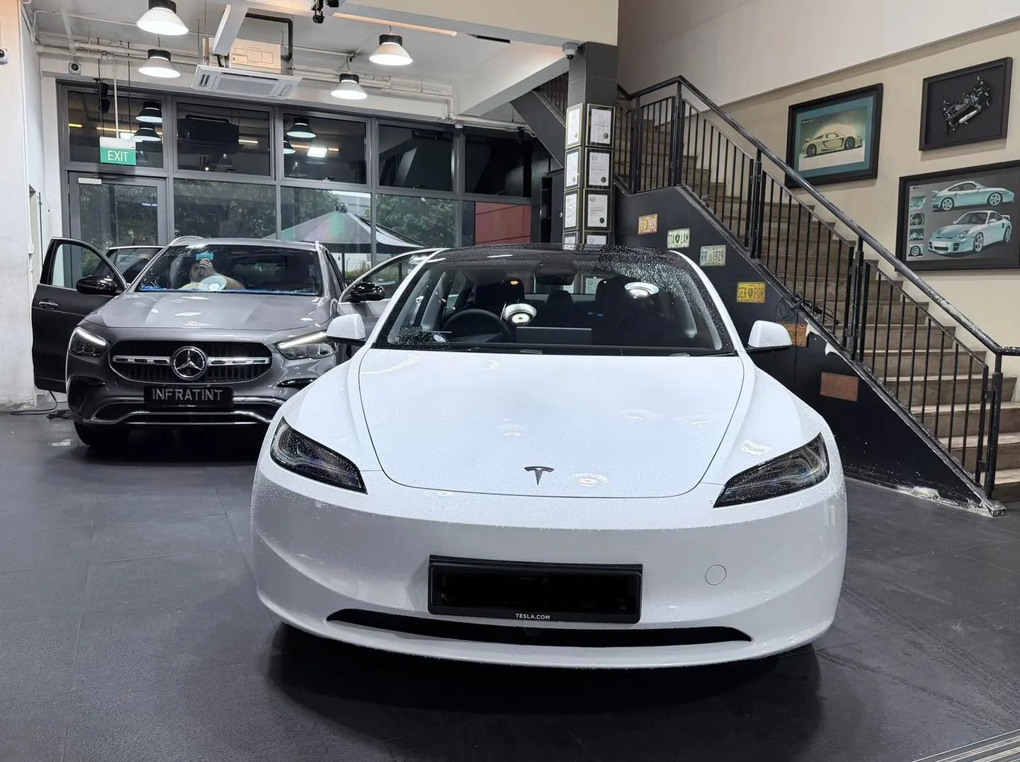 A white Tesla sedan photographed head-on indoors with an Infratint licence plate displayed.