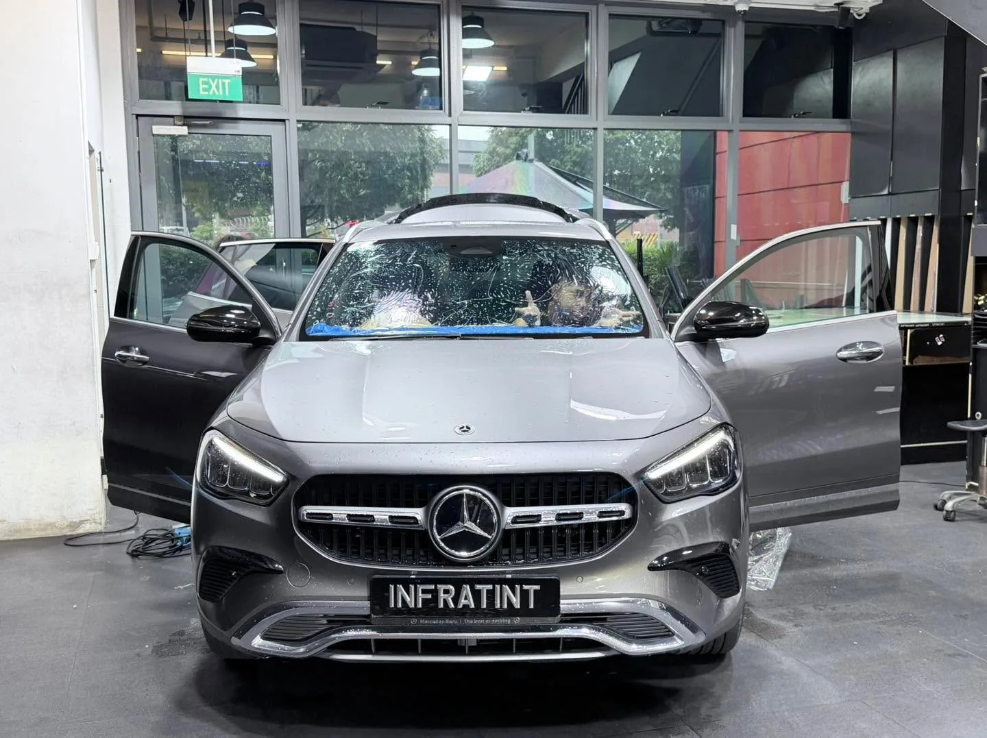A dark Mercedes-Benz sedan with doors open, photographed front-on indoors, with an Infratint licence plate.
