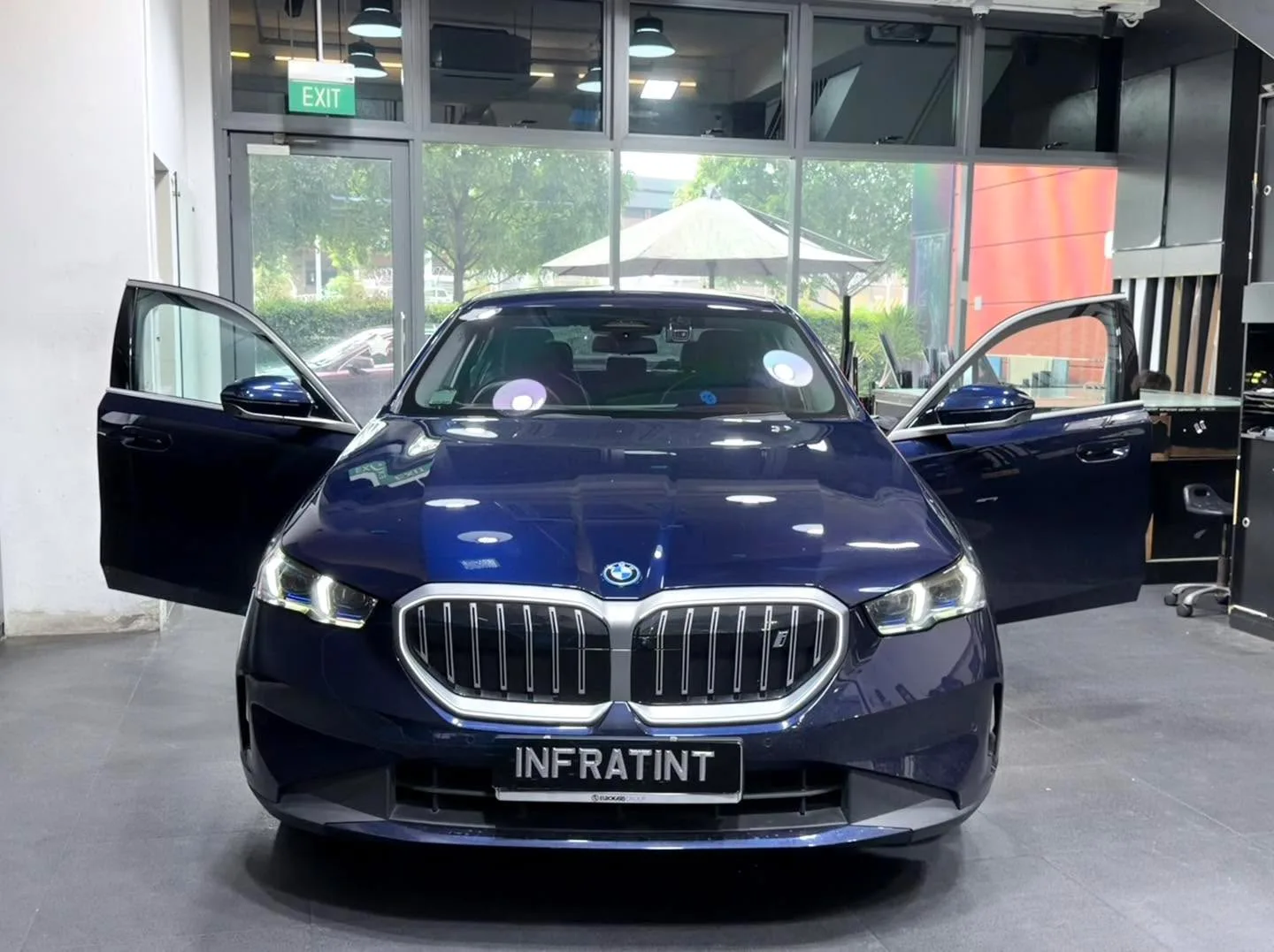 A dark blue BMW sedan photographed from the side with the driver's door open, indoors.