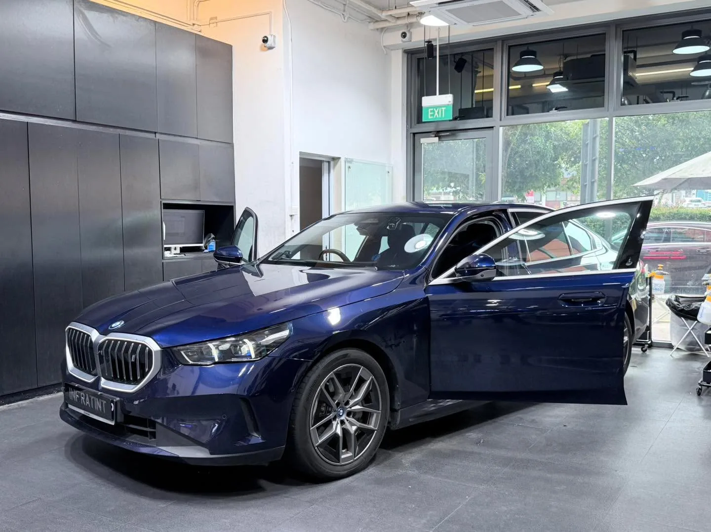 A dark blue BMW sedan photographed from the side with the driver's door open, indoors.