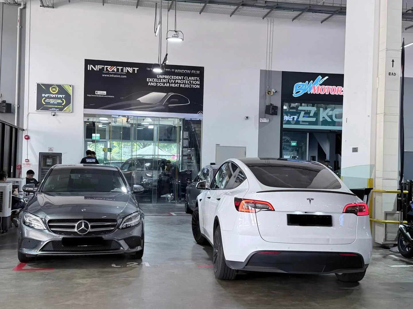A silver Mercedes-Benz saloon and a white Tesla saloon parked in the workshop.