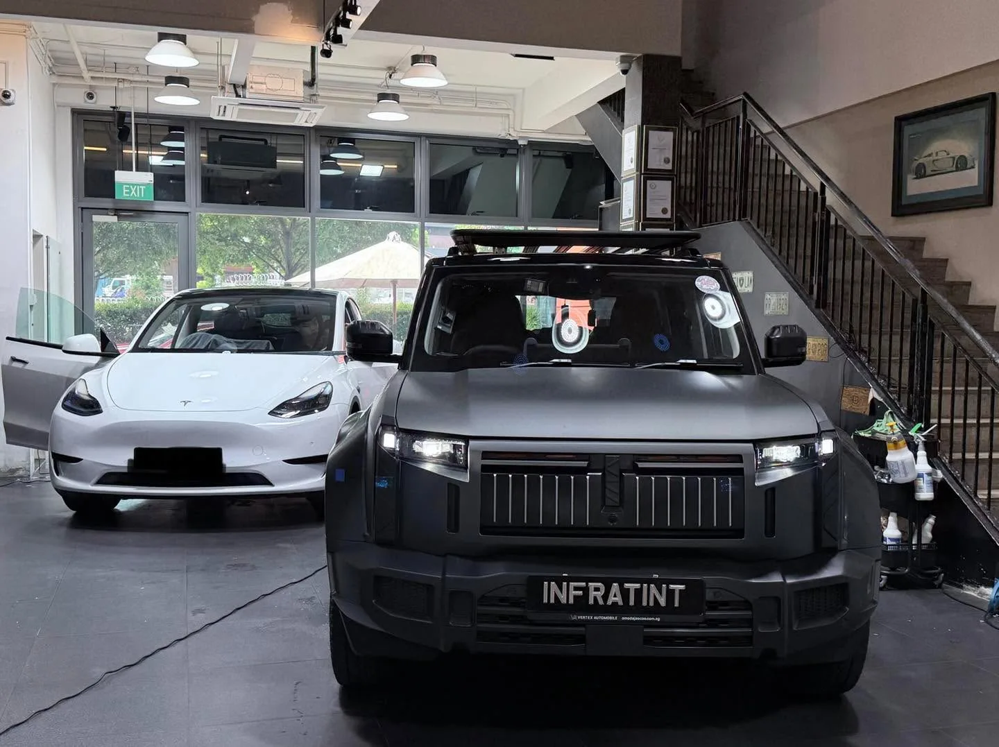 A white Tesla and a grey SUV with a roof rack parked in the showroom.