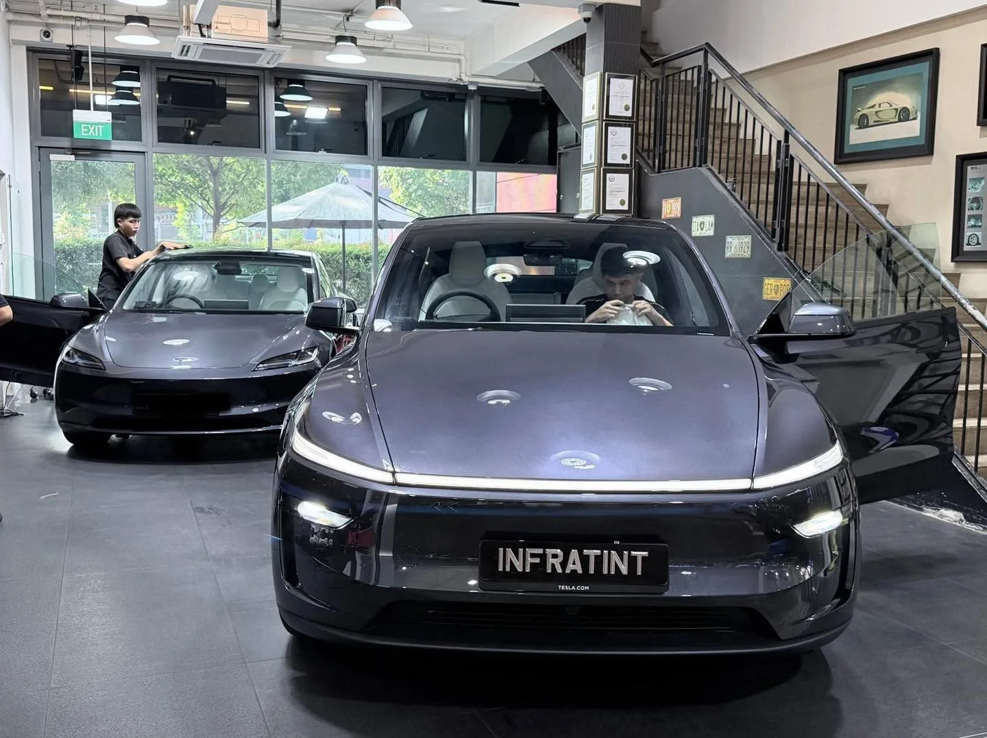 A dark-coloured Tesla saloon with its door open, parked in the showroom.