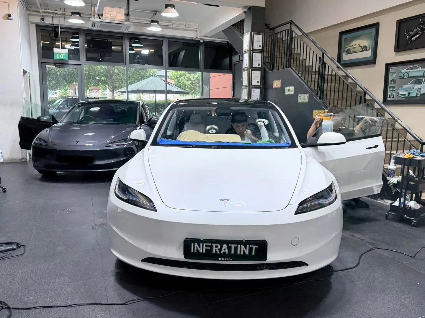 A white Tesla saloon with a door open in the workshop.