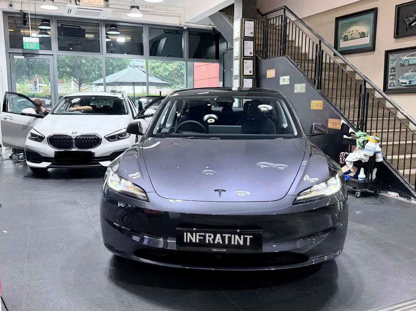A dark Tesla and a white BMW saloon parked in the workshop.
