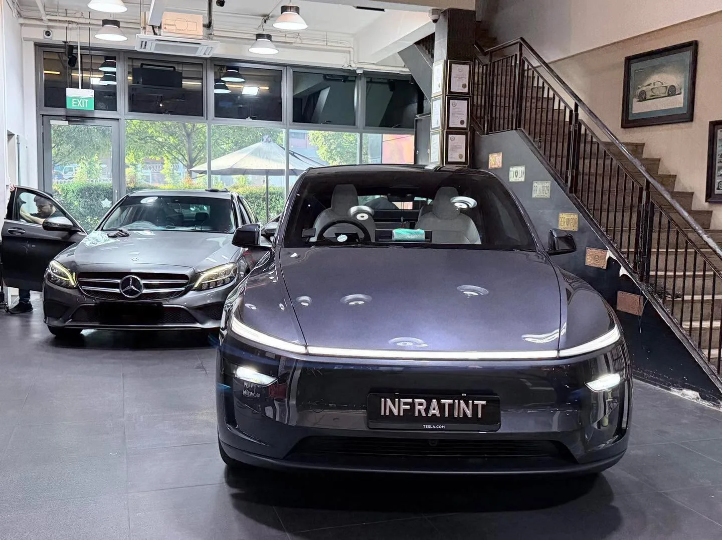 A dark Tesla saloon and a silver Mercedes-Benz saloon in the showroom.