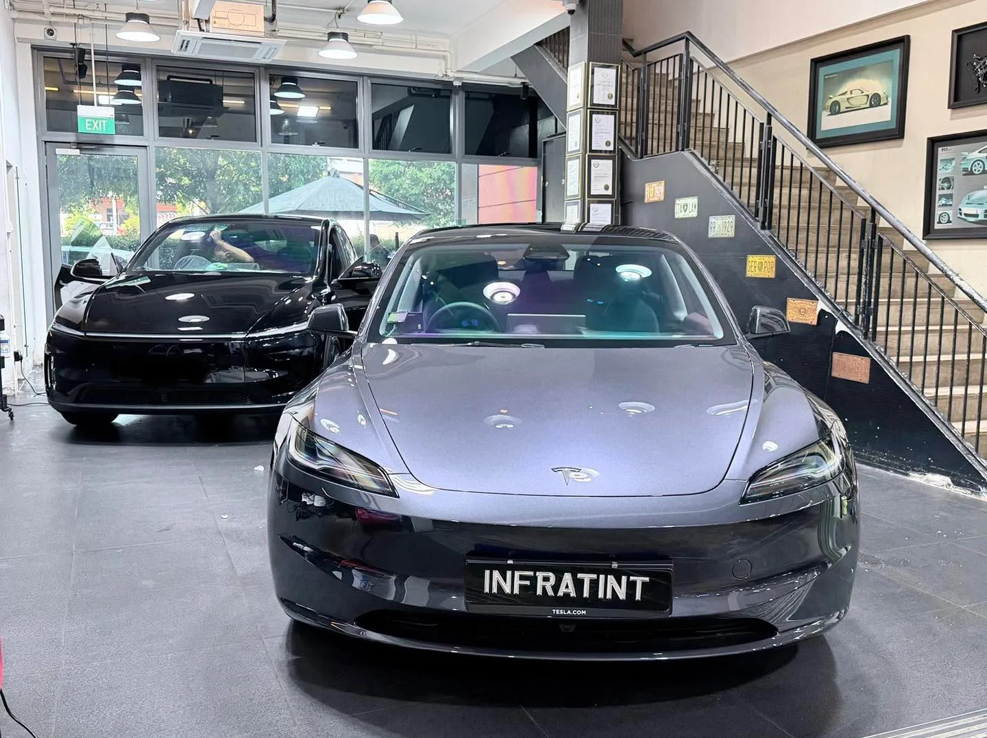 A silver Tesla and a dark Tesla parked in the workshop.