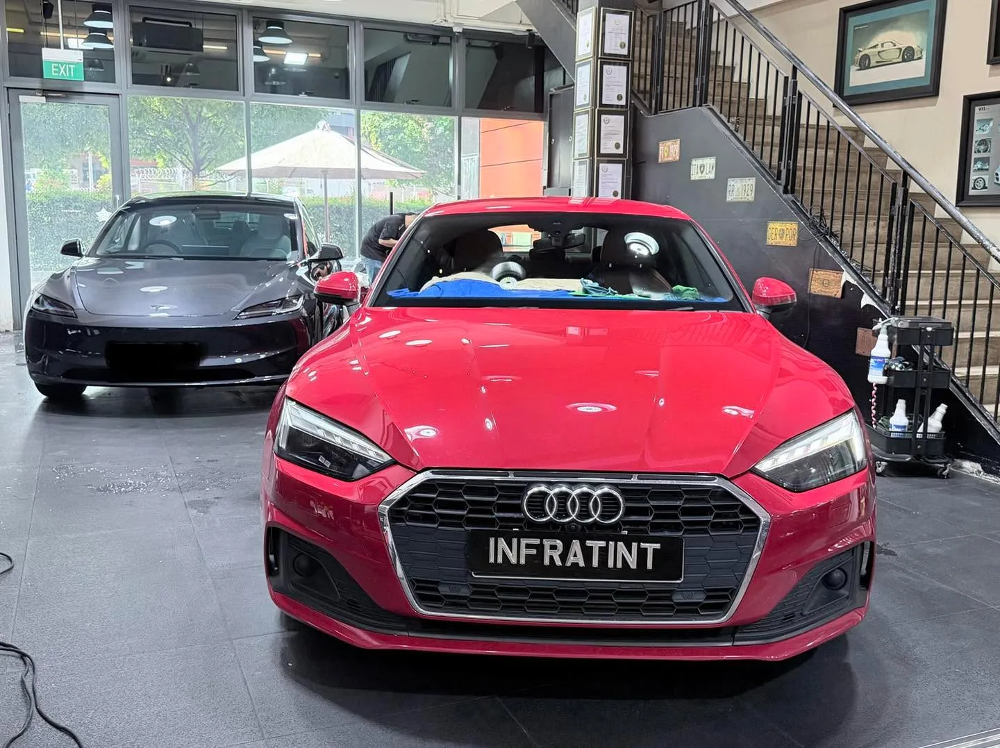 A dark Tesla and a red Audi hatchback in the showroom.