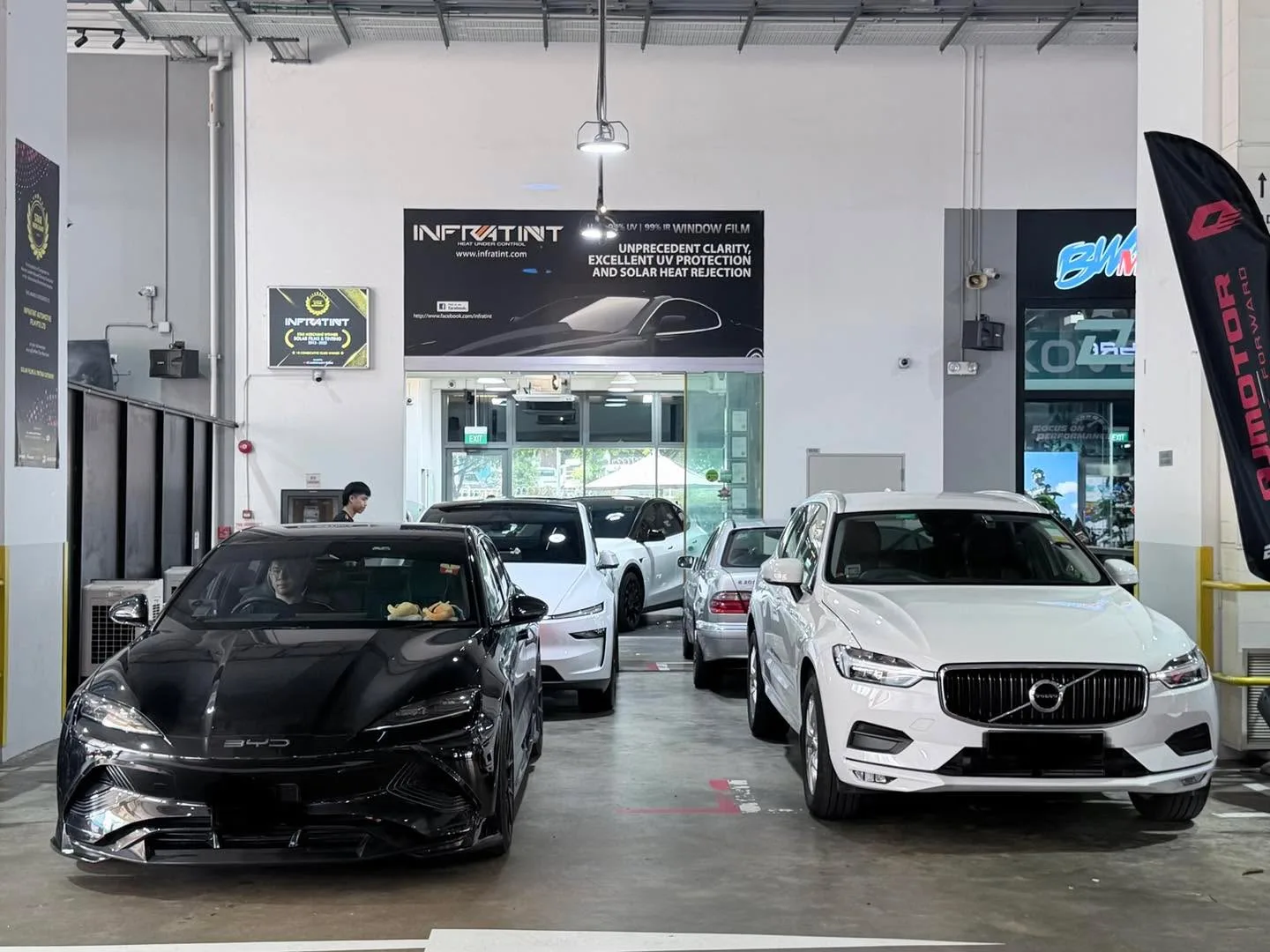 A black Tesla sedan and a white Volvo XC60 SUV parked side by side in the workshop.