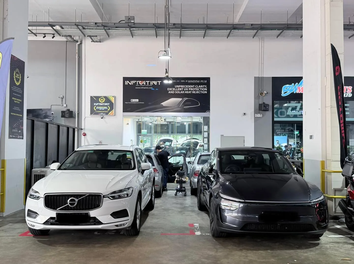 A white Volvo XC60 SUV and a black sedan parked in the workshop floor.