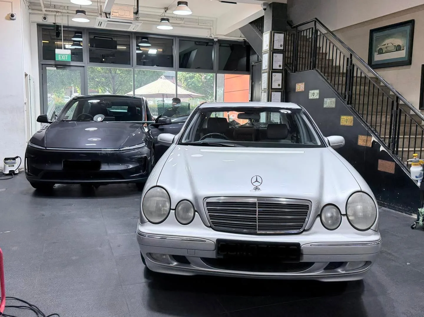 A silver Mercedes-Benz E-Class sedan and a black Tesla sedan parked indoors.