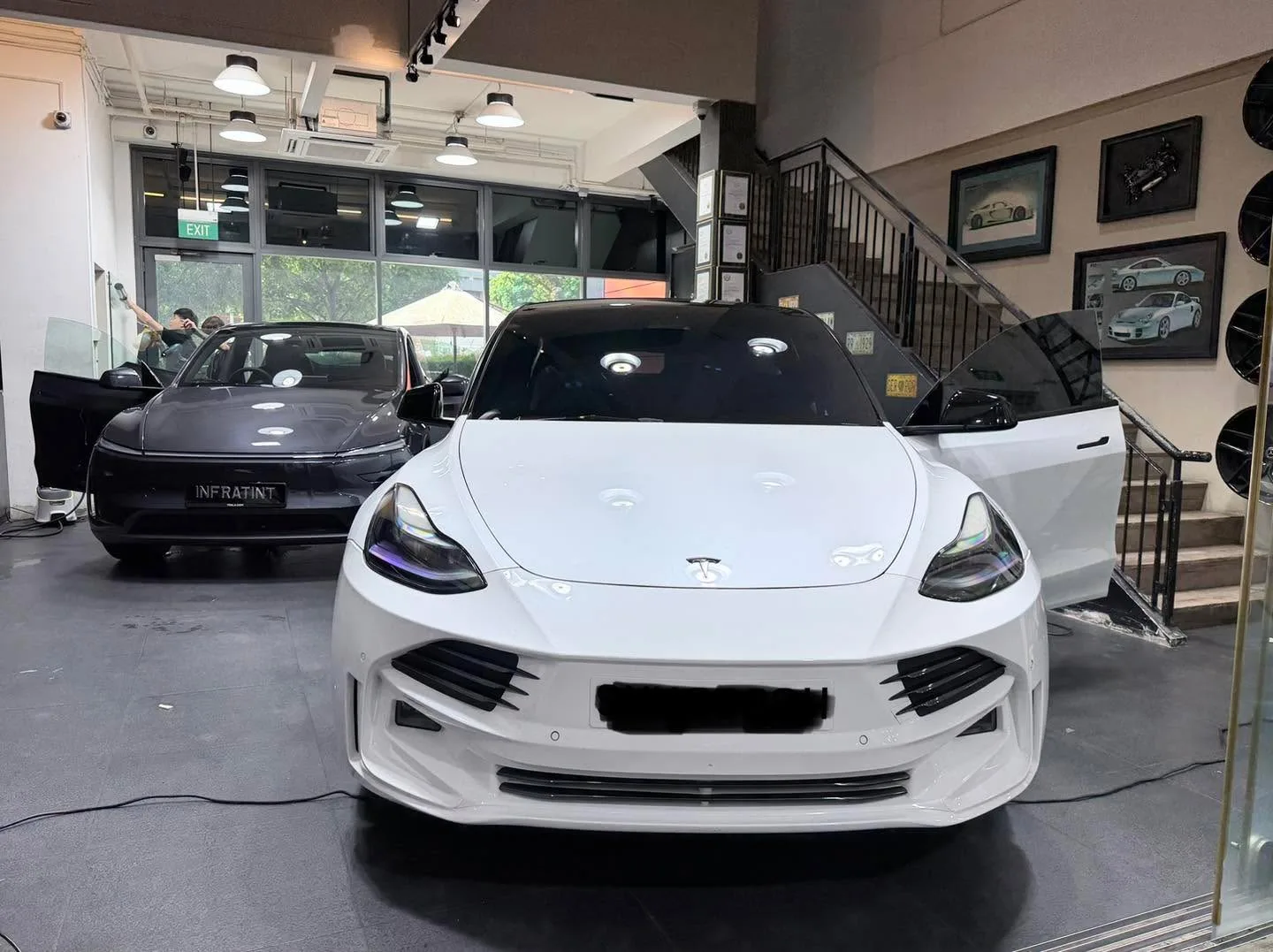 A white Tesla sedan with a black sedan and white convertible visible behind it.