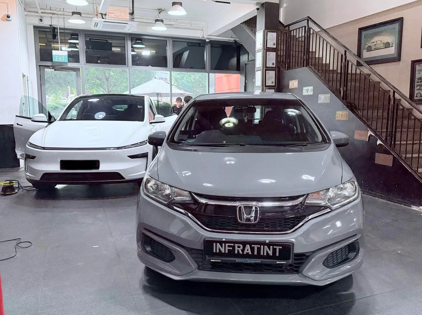 A silver Honda Fit hatchback and a white Tesla sedan parked indoors.