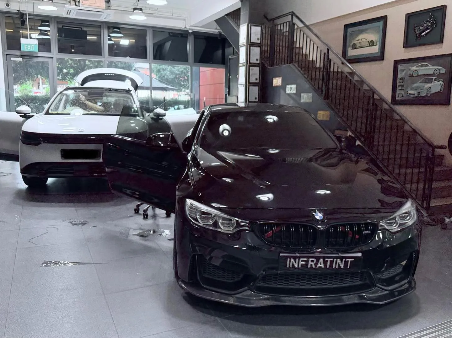 A black BMW M4 sedan and a white Tesla sedan with door open nearby.