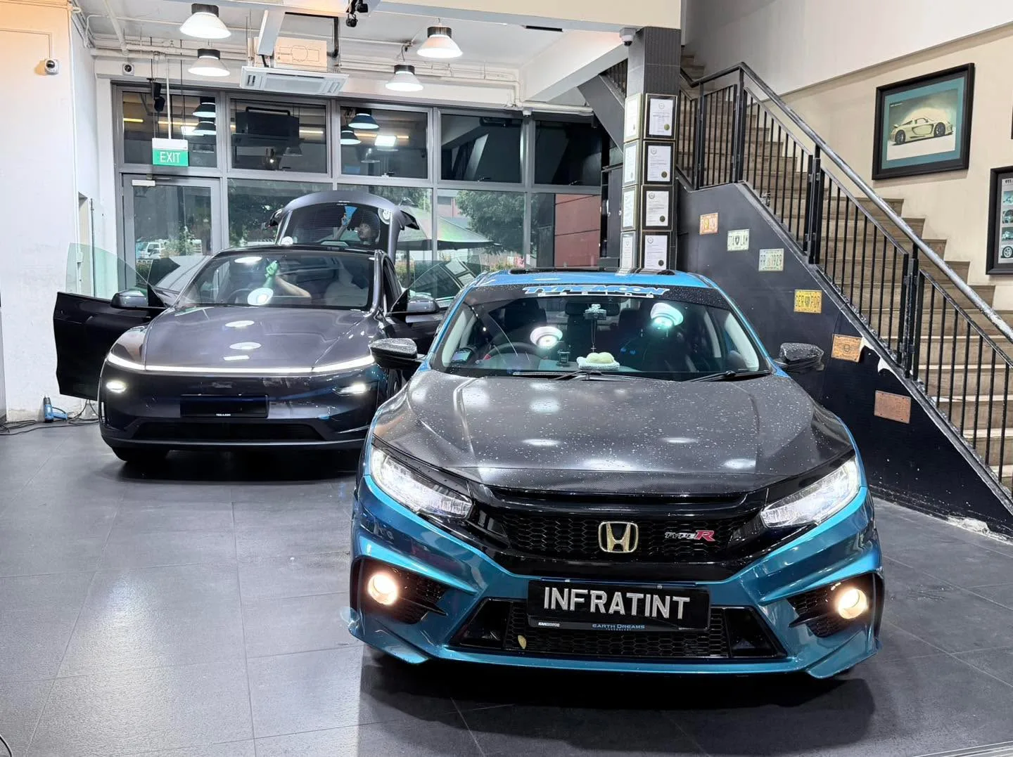 A blue Honda Civic with black roof and a black Tesla sedan parked indoors.