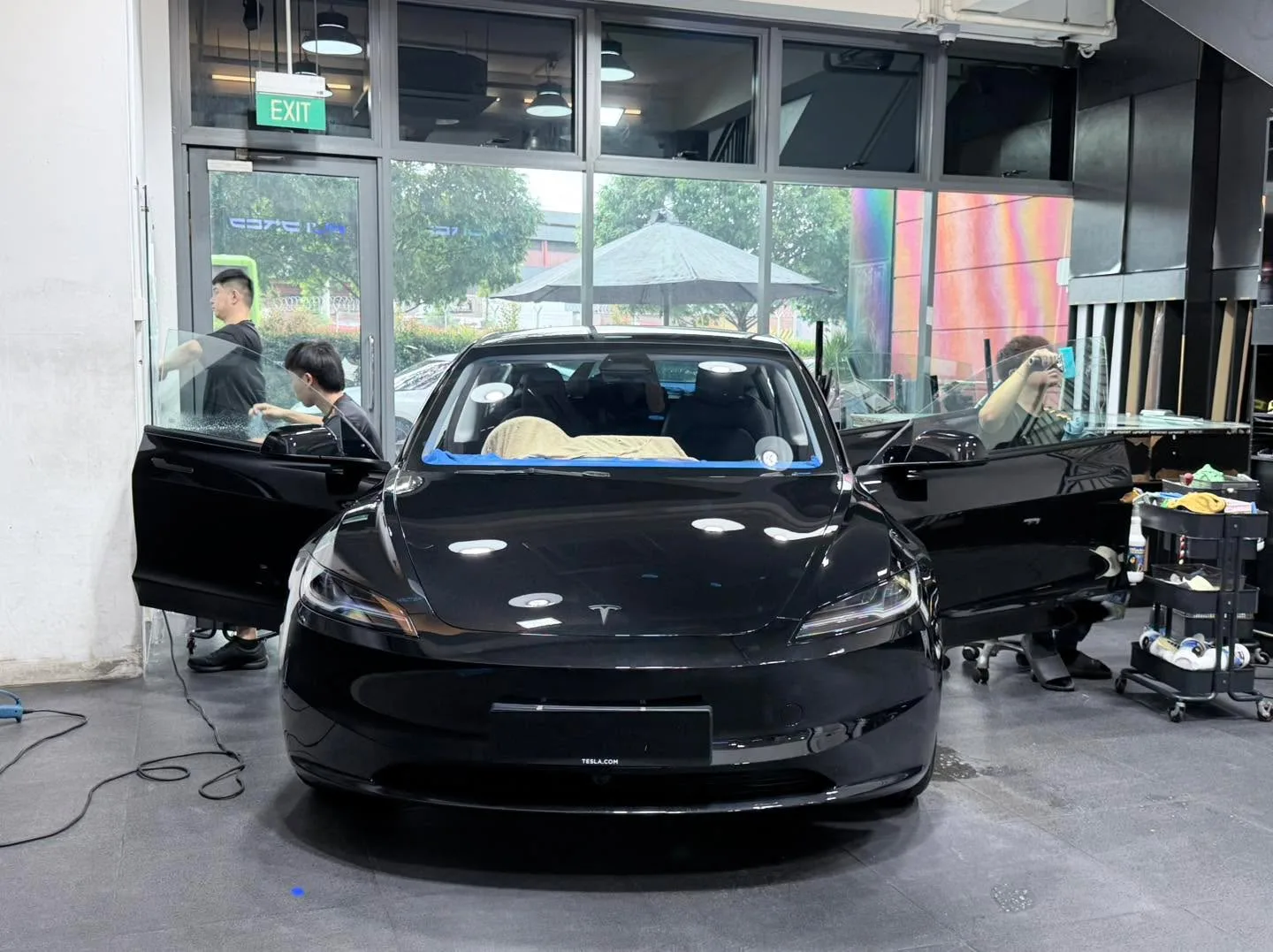 A black Tesla saloon with doors open, viewed head-on in a service bay.