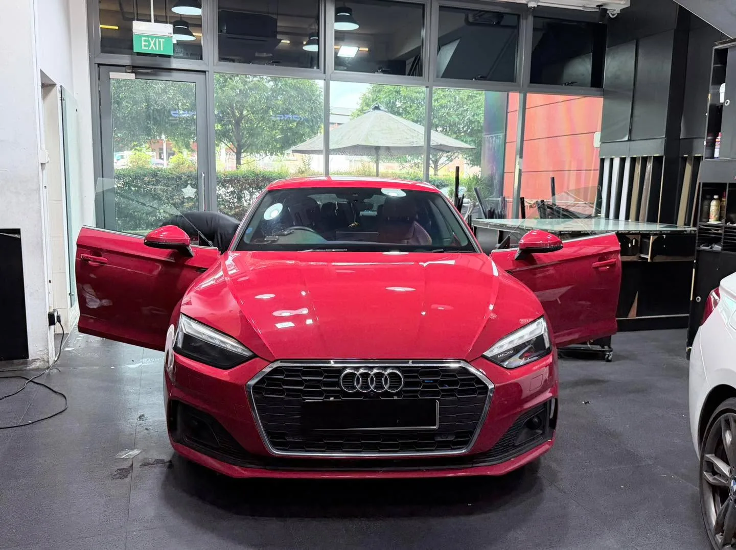 A red Audi A5 viewed from front angle with both doors open in workshop.