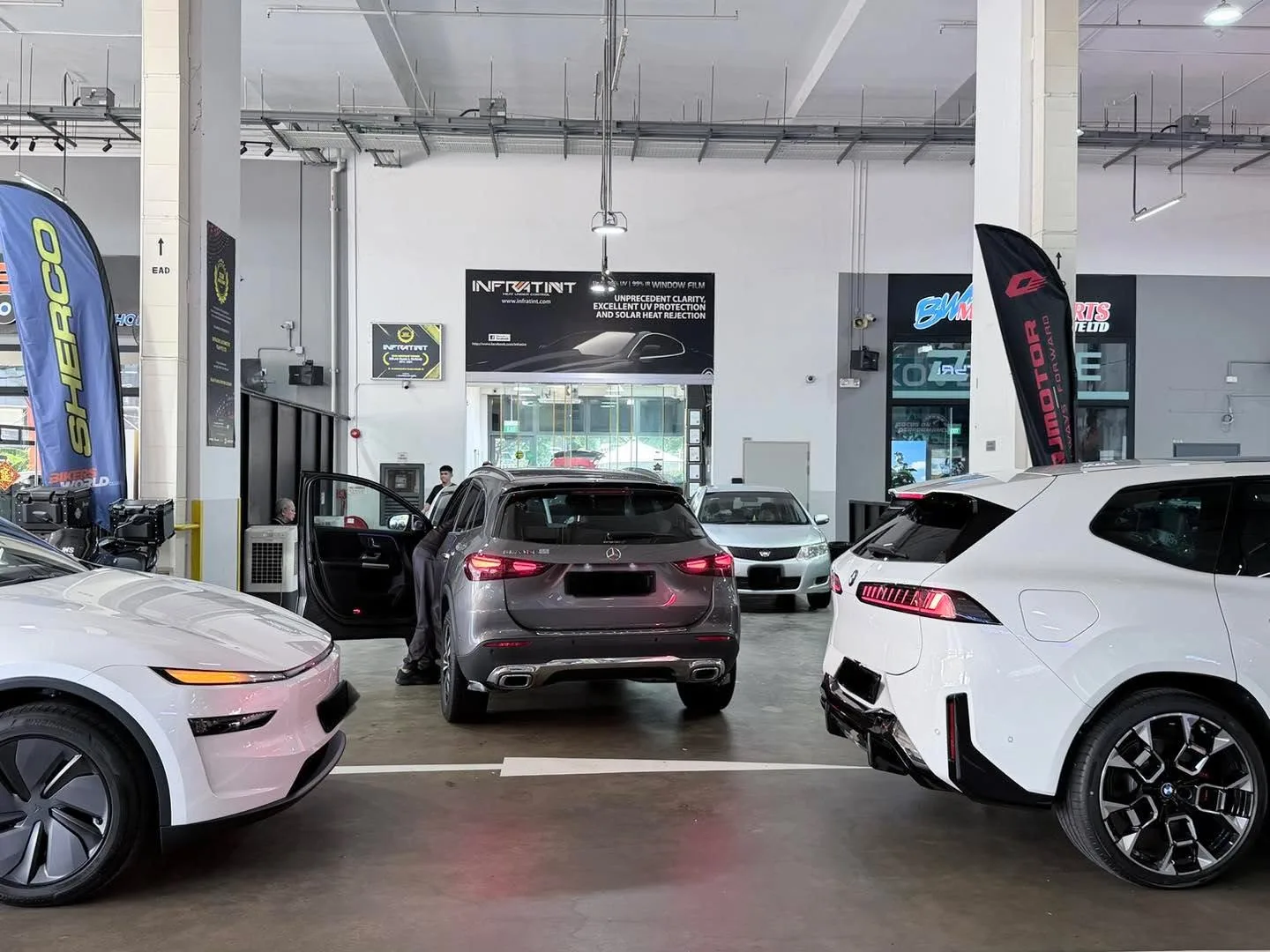A white electric coupe, a grey compact saloon, a white compact hatchback and a red sedan viewed from above in a workshop bay.