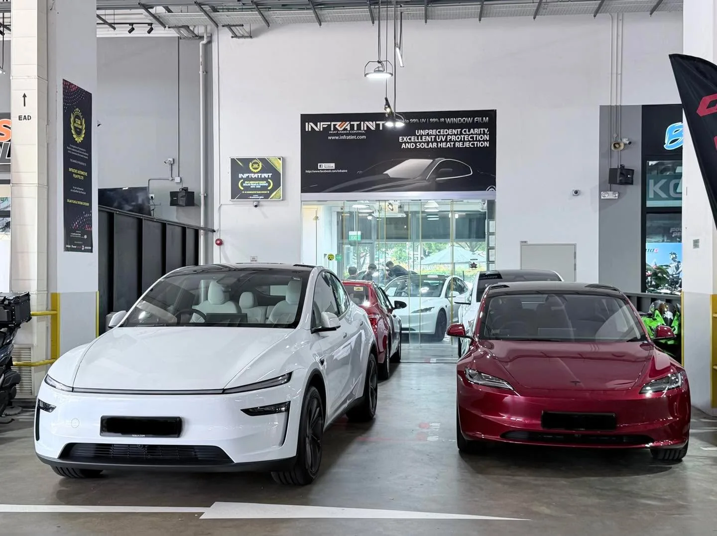 A white electric sedan and a red electric sedan parked indoors.