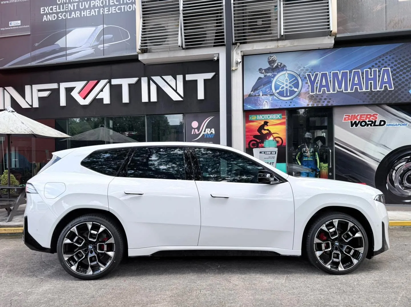 A white BMW iX3 M Sport Pro SUV with dark tinted windows, parked on a street outside the Infratint workshop.