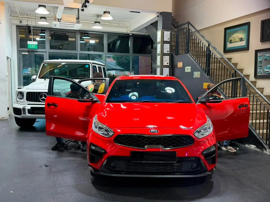 A bright red Kia Cerato compact saloon with doors open, parked indoors.