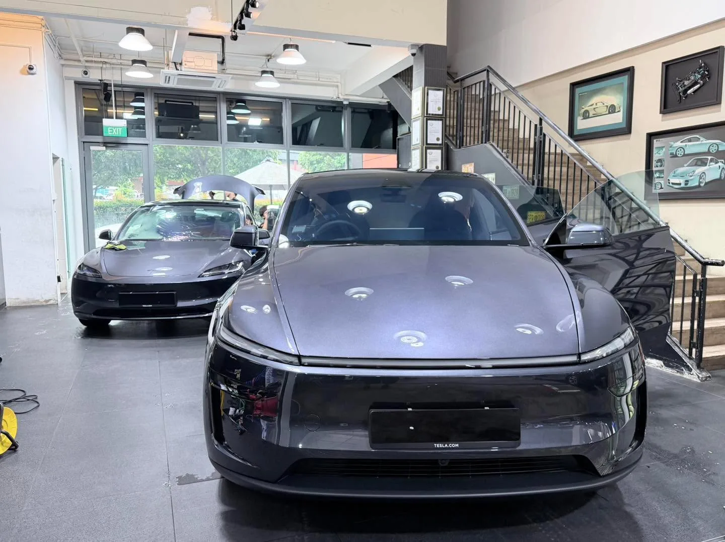 A dark grey Tesla sedan parked indoors, clearly showing the Tesla.com badge.
