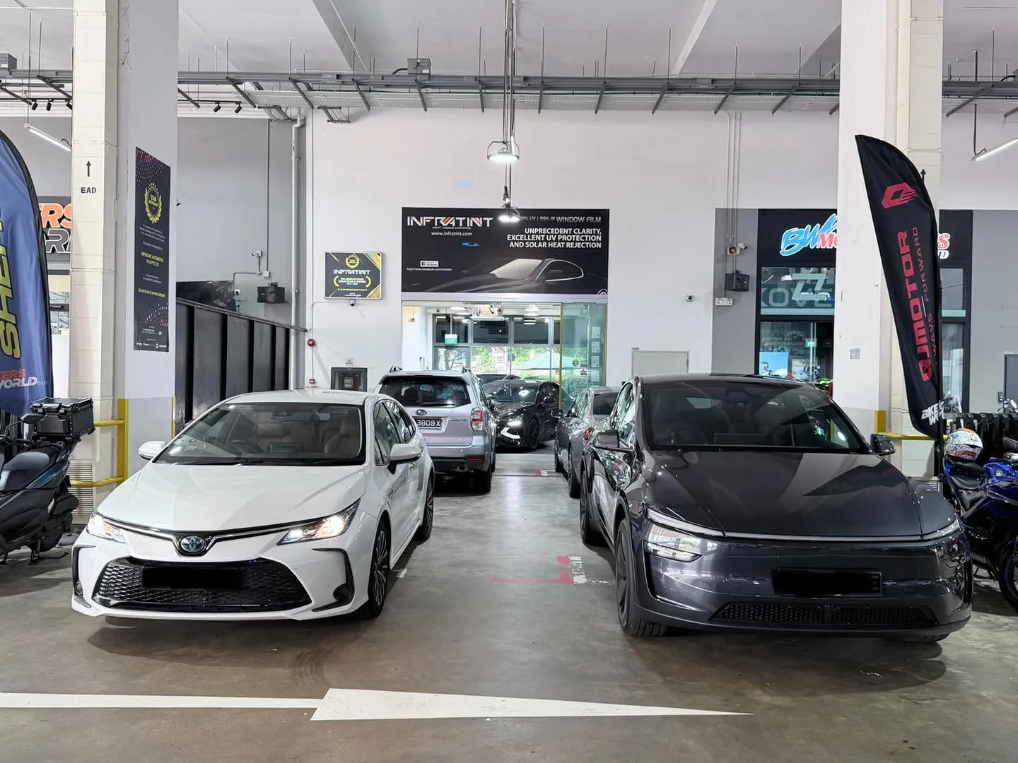 A white Toyota Altis and a black car parked side by side in the workshop.