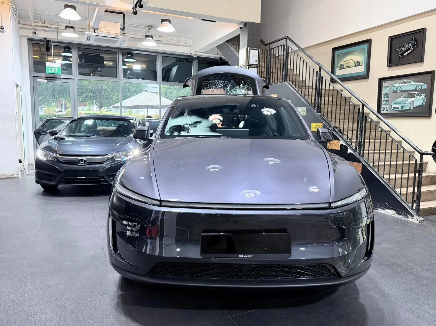 A dark grey Tesla electric saloon photographed from the rear in the workshop.