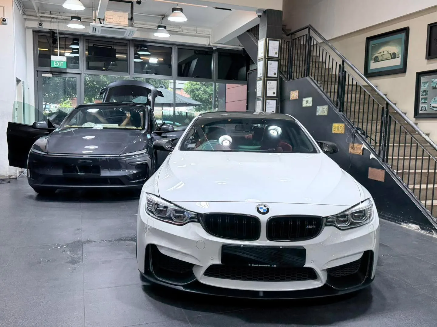 A white BMW M4 performance saloon and a dark car parked in the workshop.