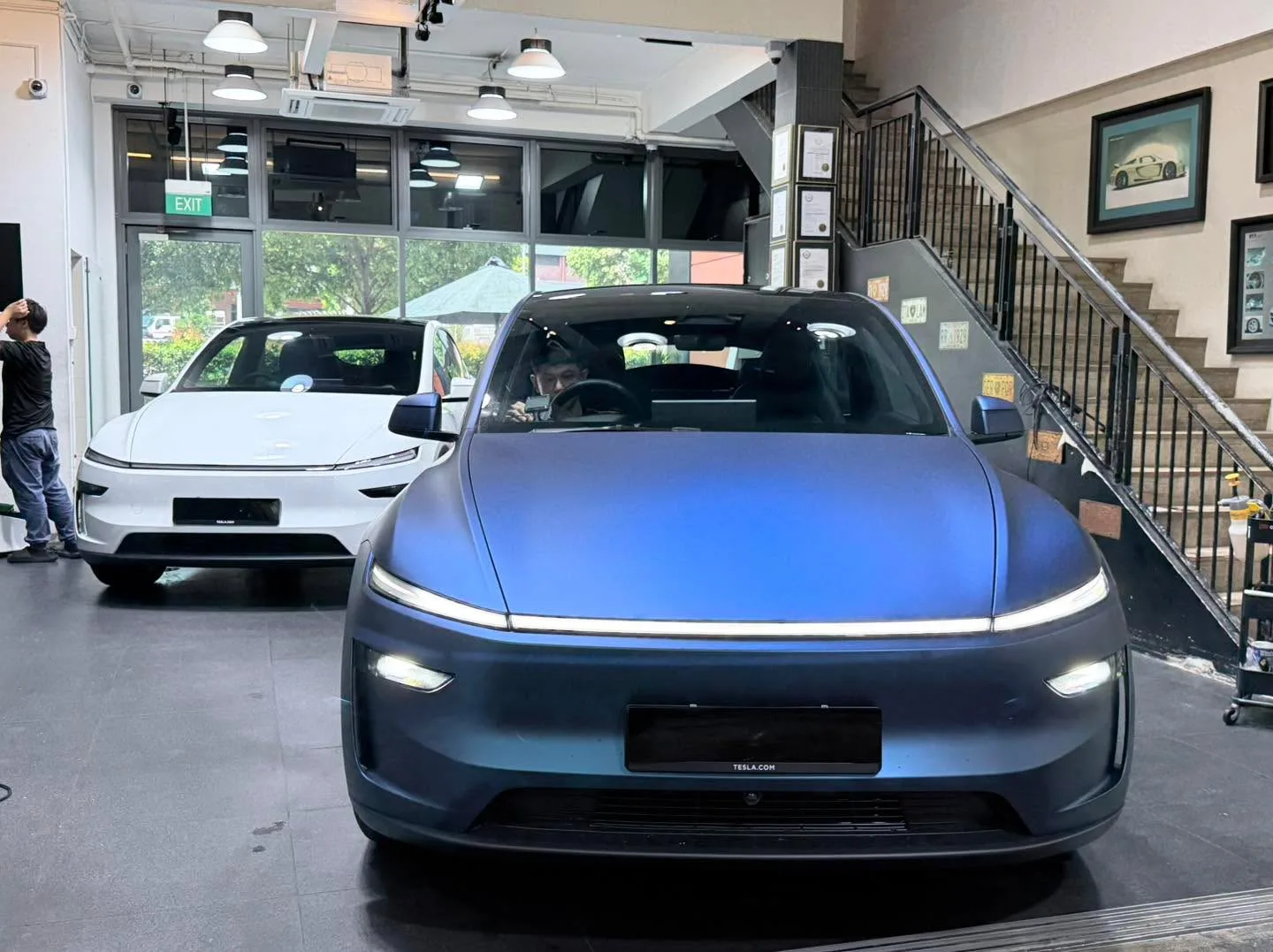 A white Tesla electric saloon and a blue car parked in the workshop.