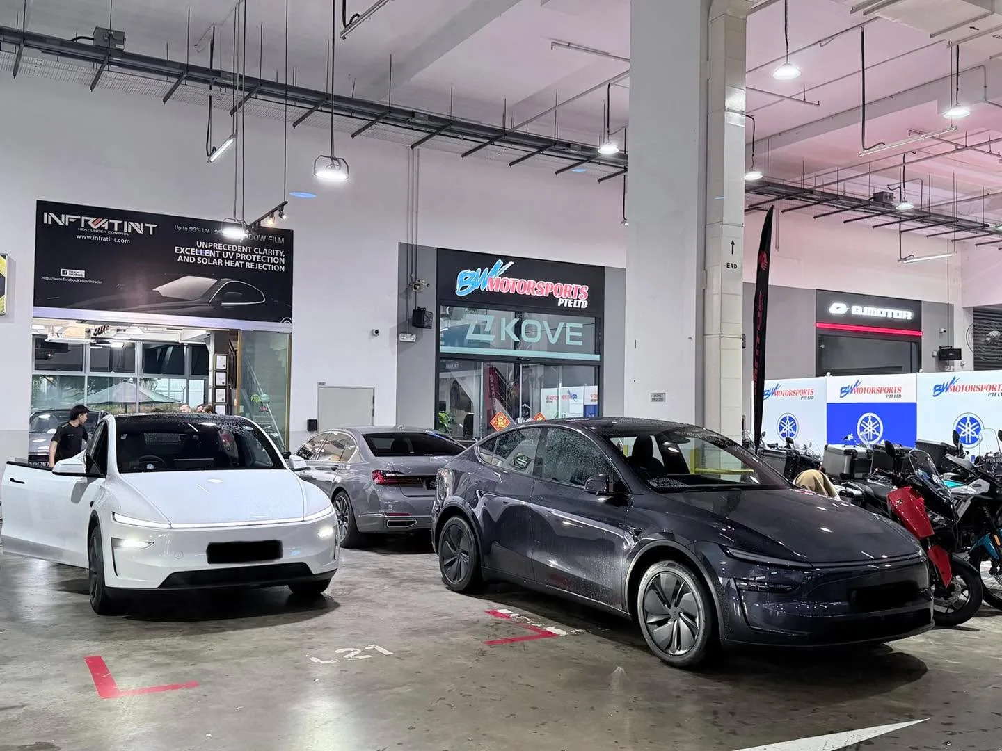 A white Tesla and a dark sedan parked in the workshop alongside other cars near the Infratint storefront.