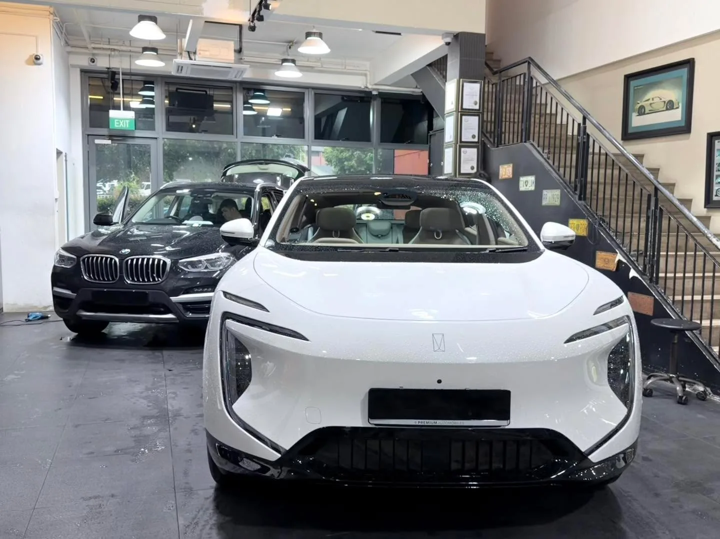 A white sedan and a dark BMW SUV parked indoors in the workshop.