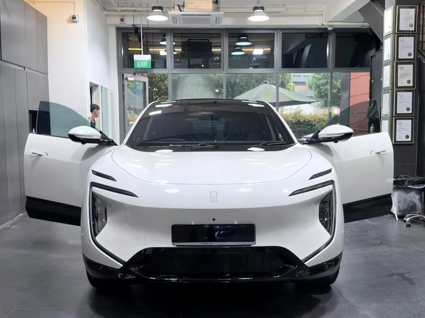 A white electric sedan with distinctive grille design, doors open, viewed head-on in the workshop.