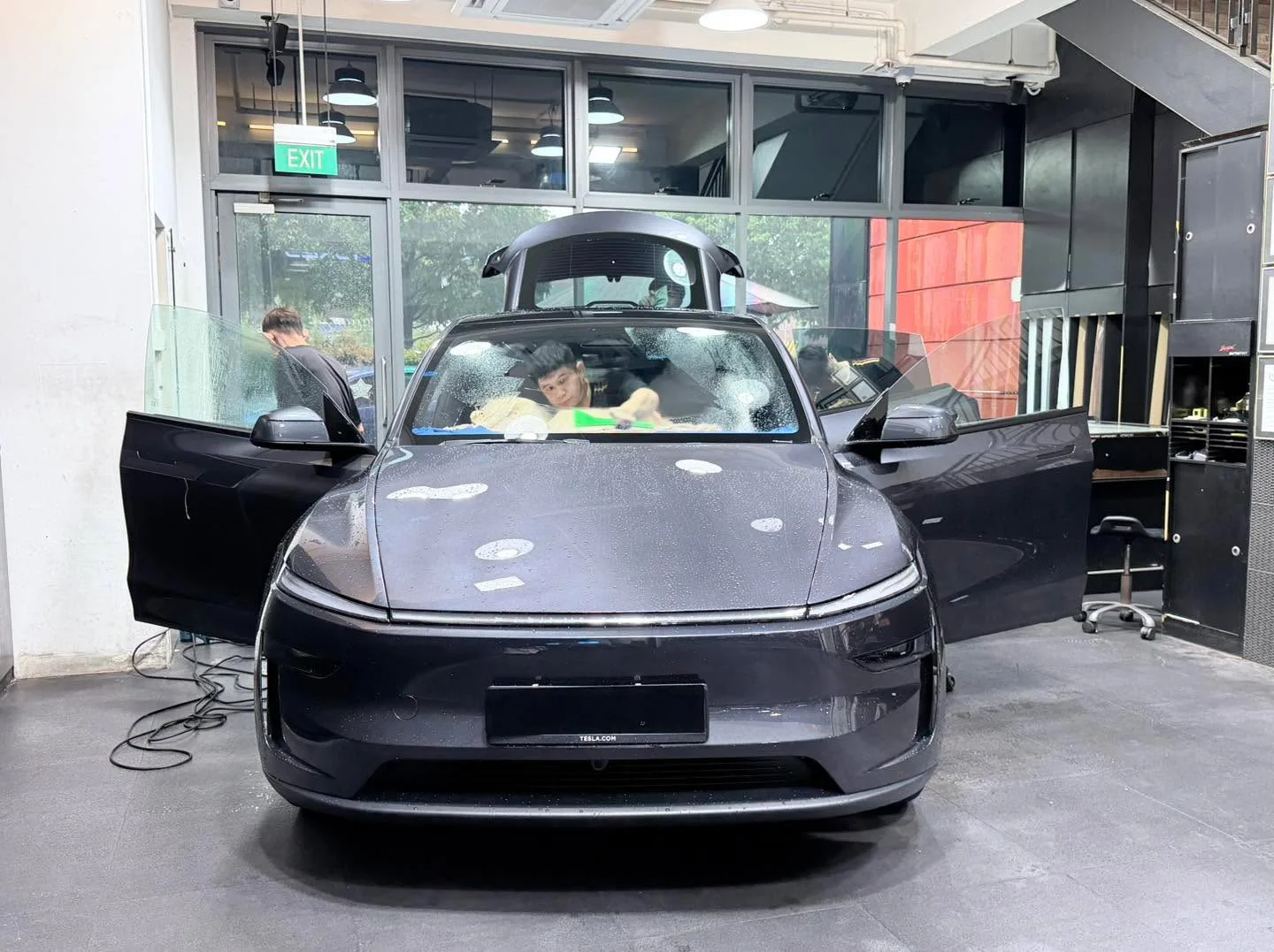 A dark purple electric sedan with gull-wing door open, people visible inside the workshop.