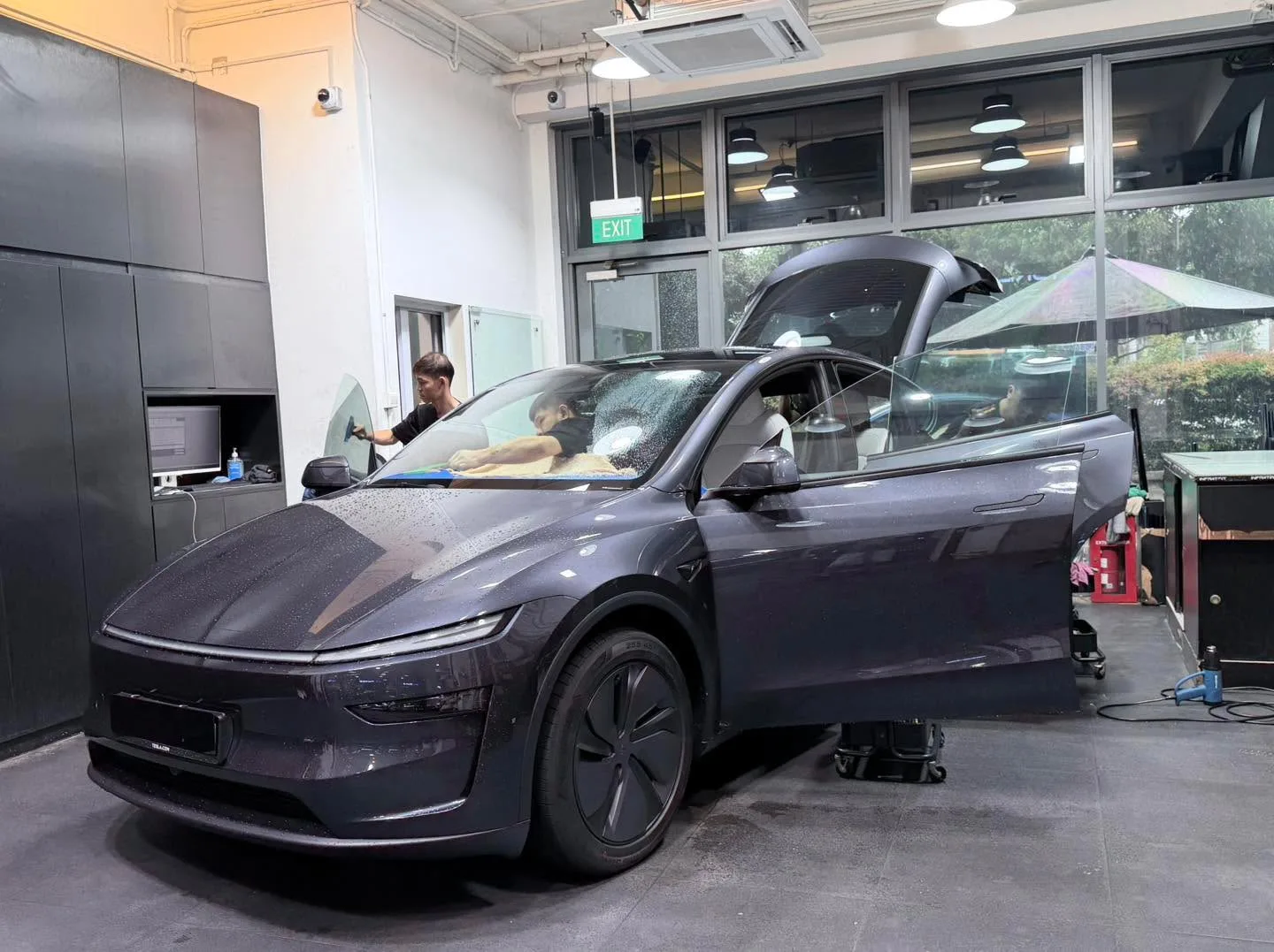 A dark purple electric sedan with door open, technicians working on the windows.