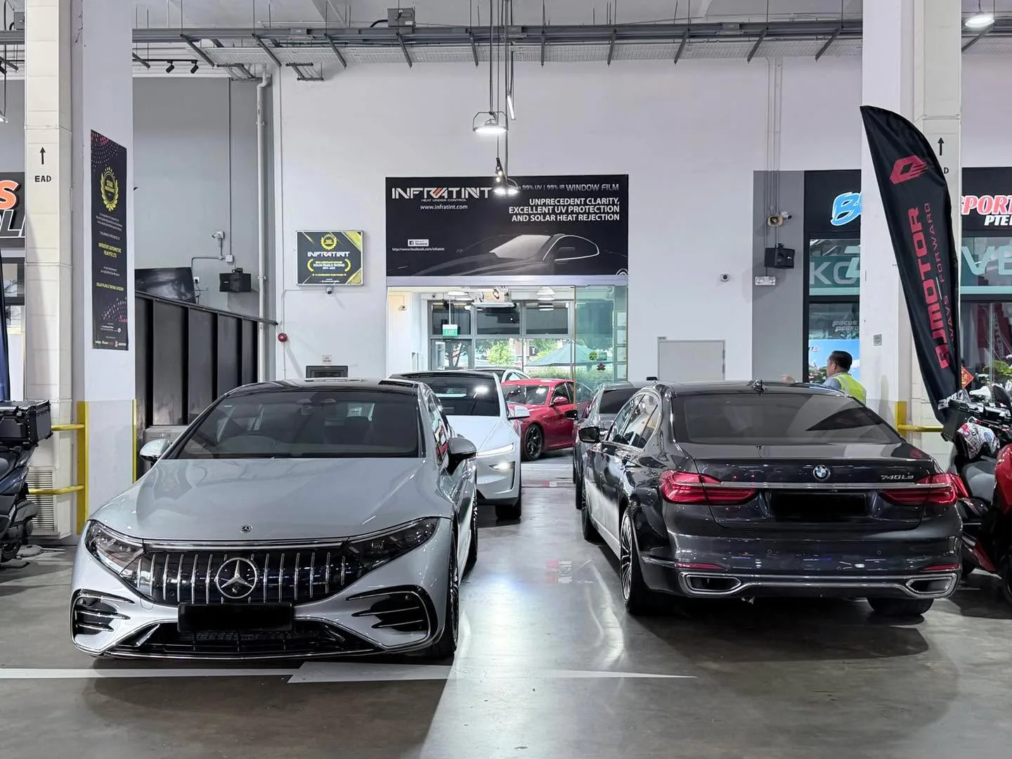 A silver Mercedes-Benz with a distinctive grille and a black BMW sedan parked inside the workshop.