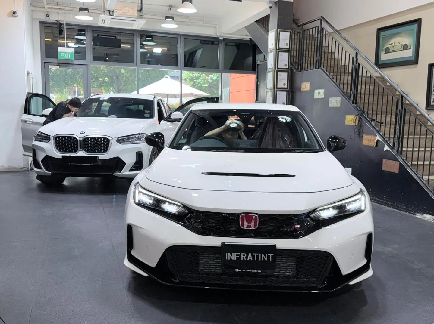 A white Honda Civic and a white BMW X3 with doors open inside the workshop.